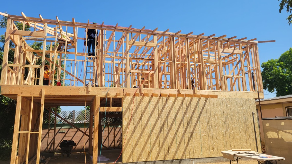 Two-story new build framing with worker on top under blue sky