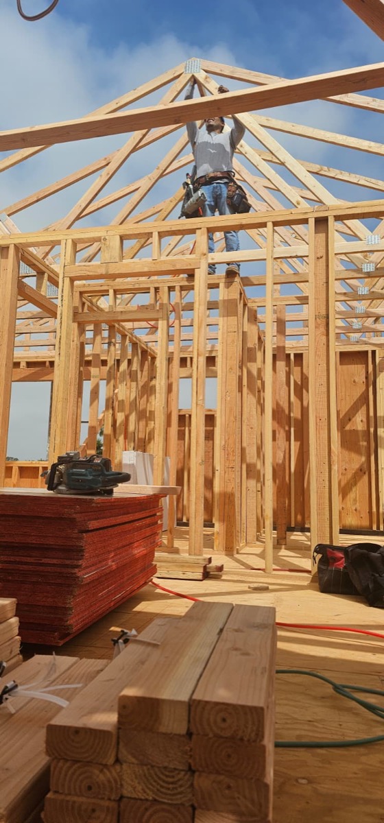 Framing worker on peaked roof structure against blue sky